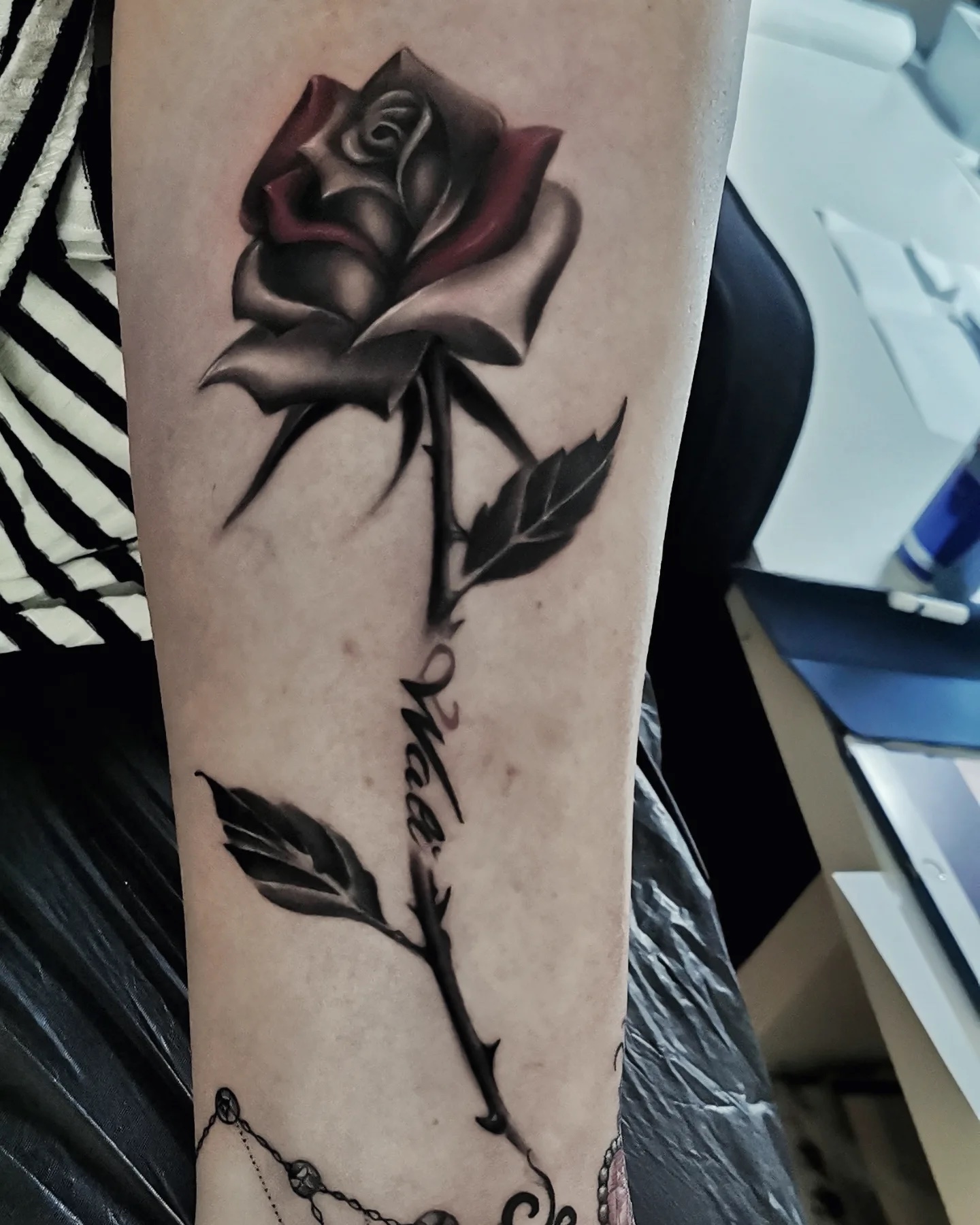 Rose in black, grey, and red on the forearm